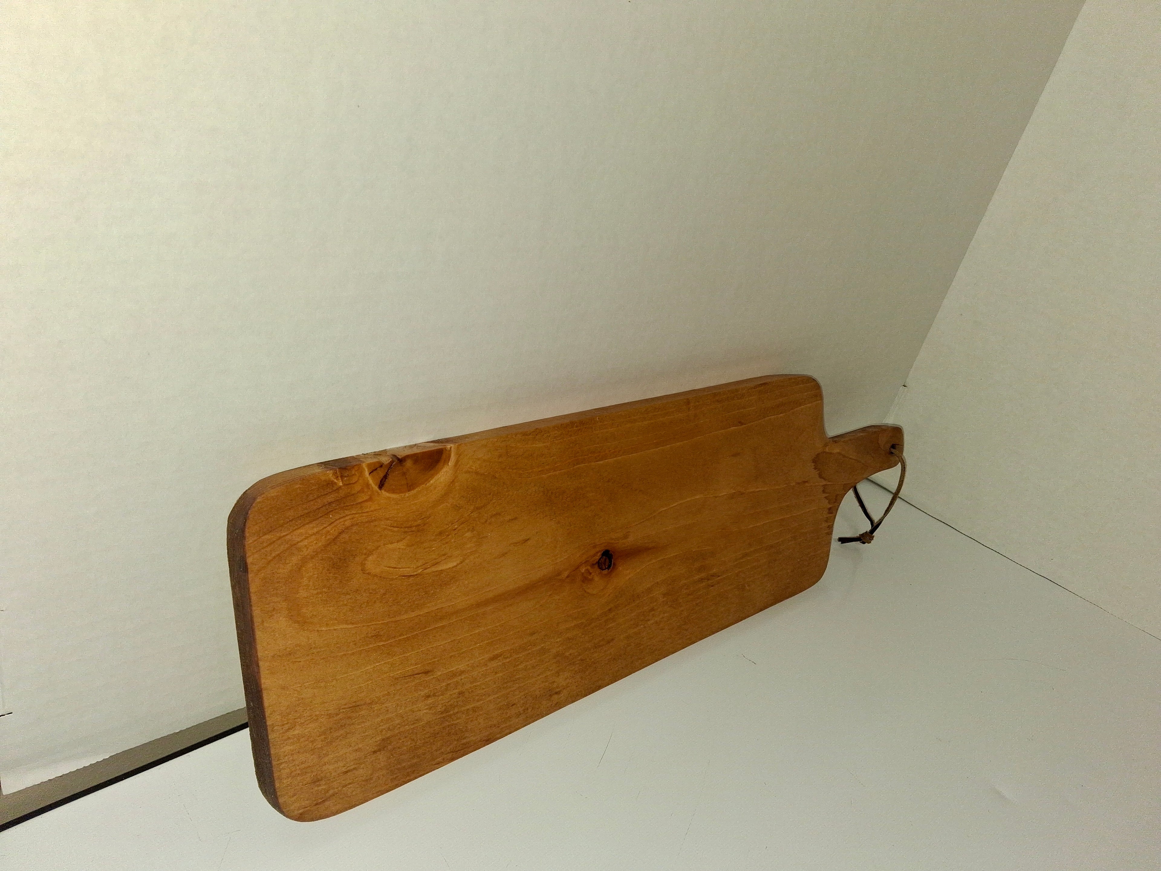Handmade rustic paddle-style charcuterie serving board with leather cord loop on handle