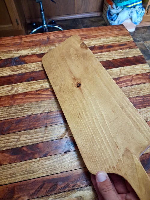 Close-up of handmade wood serving board showing natural grain and knots, displayed on rustic wood surface